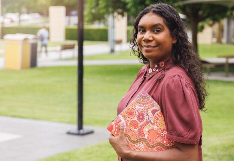 image showing young Aboriginal woman holding folder standing outdoors, to illustrate First Nations Cadetship Program