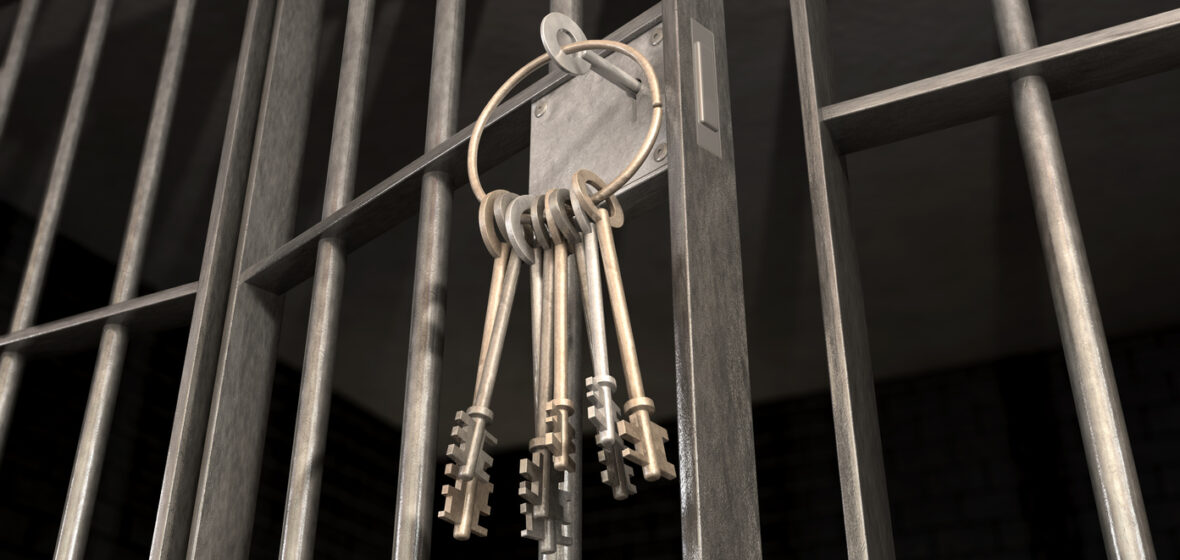 A closeup of the lock of a jail cell with iron bars and a bunch of key in the locking mechanism with the door open to show prison life