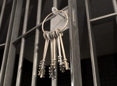 A closeup of the lock of a jail cell with iron bars and a bunch of key in the locking mechanism with the door open to show prison life