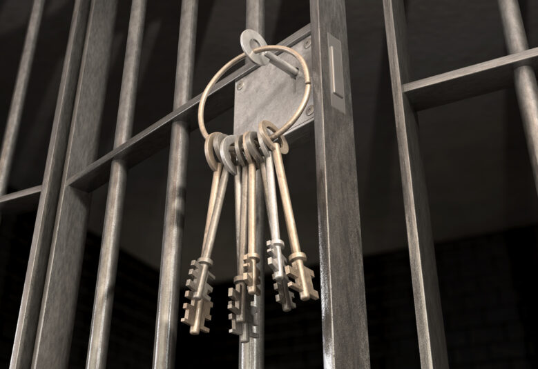 A closeup of the lock of a jail cell with iron bars and a bunch of key in the locking mechanism with the door open to show prison life