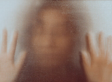 photo showing woman behind mottled glass with hands up